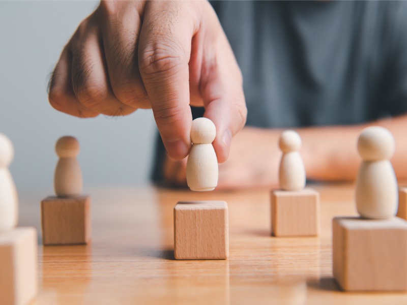 Hand placing a wooden person onto a wooden block